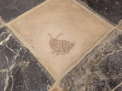 In eine helle Steinplatte im Boden einer Kirche eingravierte Zeichnung der Steinlaus: ein rundliches Fantasietier mit Fühlern, großen Zähnen und sechs Beinen.